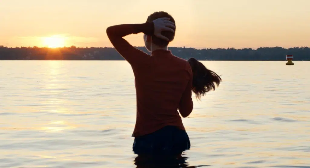 Netflix: confira as novidades para março! Uma jovem está em pé dentro de um rio, com a água chegando quase à altura da cintura, de costas para a câmera. Ela olha o horizonte.