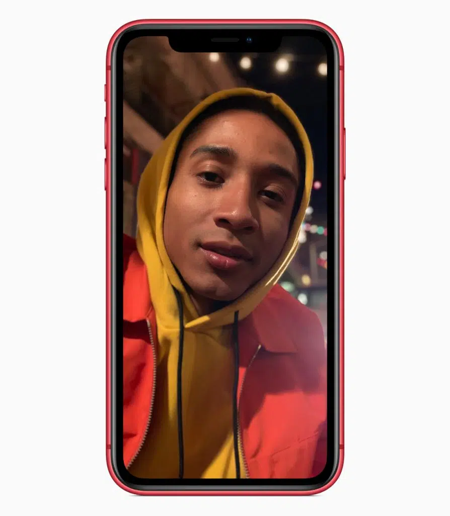 Iphone se 2020 ou iphone xr: qual o melhor modelo de entrada da apple? Imagem mostra um iphone xr vermelho exibindo a foto de um jovem negro com a cabeça coberta pelo capuz de um moletom amarelo mostarda e jaqueta vermelha sobreposta. A foto foi tirada usando modo retrato, por isso o fundo está desfocado.