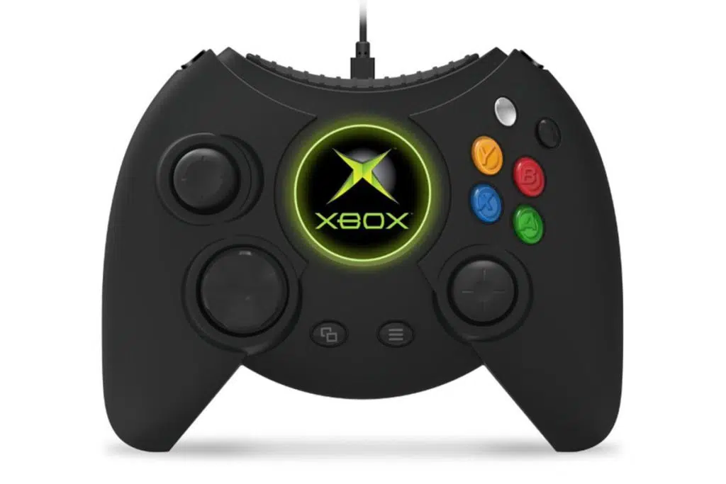 Utvecklingen av Xbox: Hur Microsoft-konsolen blev en jätte i spelbranschen Duke control står med vit bakgrund. Kontrollen är belagd i svart och knapparna på höger sida innehåller några färger, som blått och rött. I mitten finns xbox-logotypen markerad i grönt.