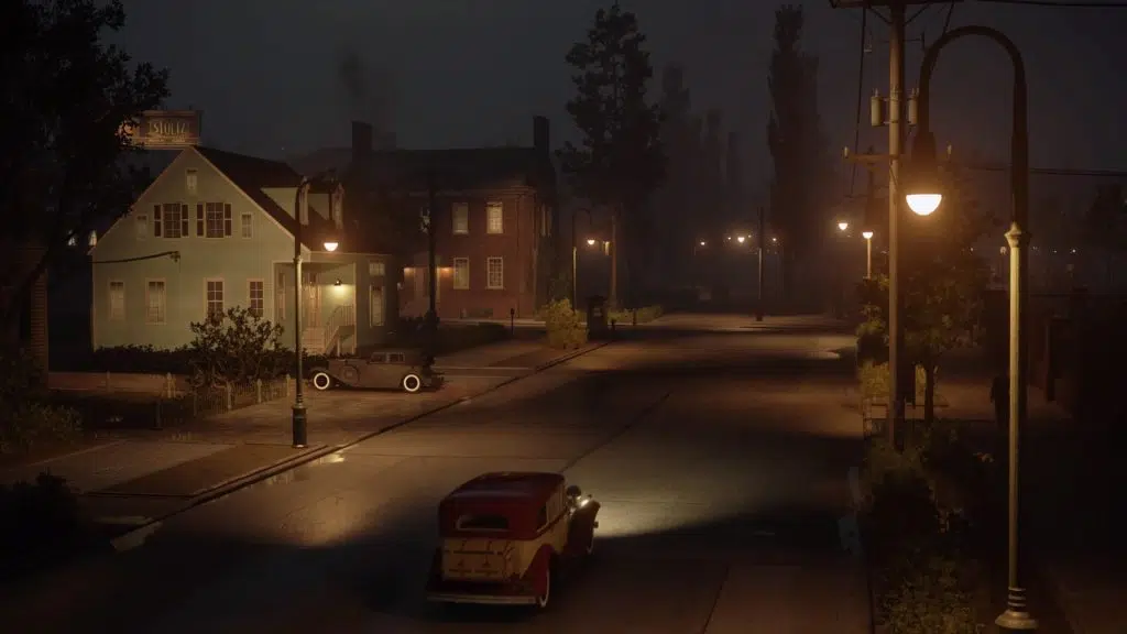 Review: mafia: definitive edition, nova roupagem para um jogo antigo Vista aérea de um carro se aproximando de casas à noite.