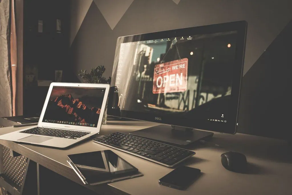 Cómo conectar su computadora portátil a un monitor Sobre la mesa, computadora, celular, tablet y una notebook; el último, transmitiendo una imagen al monitor de la computadora para ilustrar cómo conectar su computadora portátil a un monitor