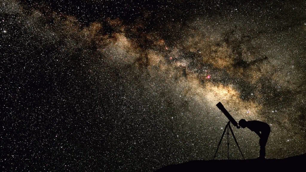 10 cursos online mais legais na khan academy Pessoa olhando um céu estrelado através de uma luneta.