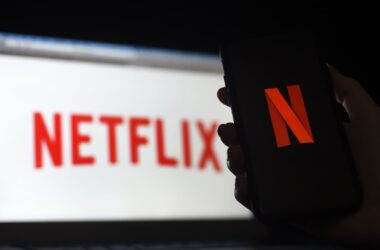 Logo da netflix em um celular, na frente de uma tela branca