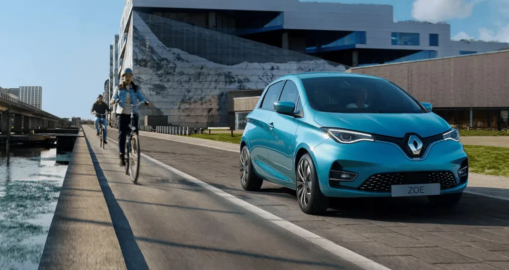 Carros elétricos e condomínios: como fica o ponto de carregamento? Imagem de divulgação de um renault zoe e-tech azul em uma rua ao lado de dois ciclistas.