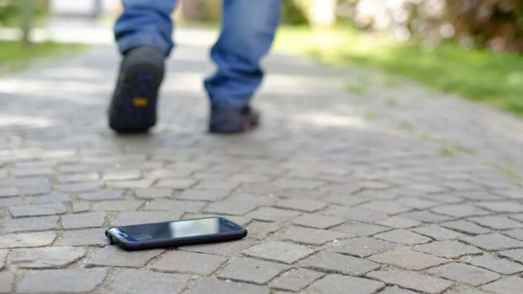 Celular roubado? Veja como bloquear chip e recuperar o número Pessoa andando e deixando um smartphone no chão, esquecido, para ilustrar um smartphone perdido.
