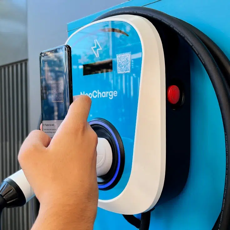 Carros elétricos e condomínios: como fica o ponto de carregamento? Mão segurando um smartphone tentando focar no qr code da estação de carregamento de carro elétrico.