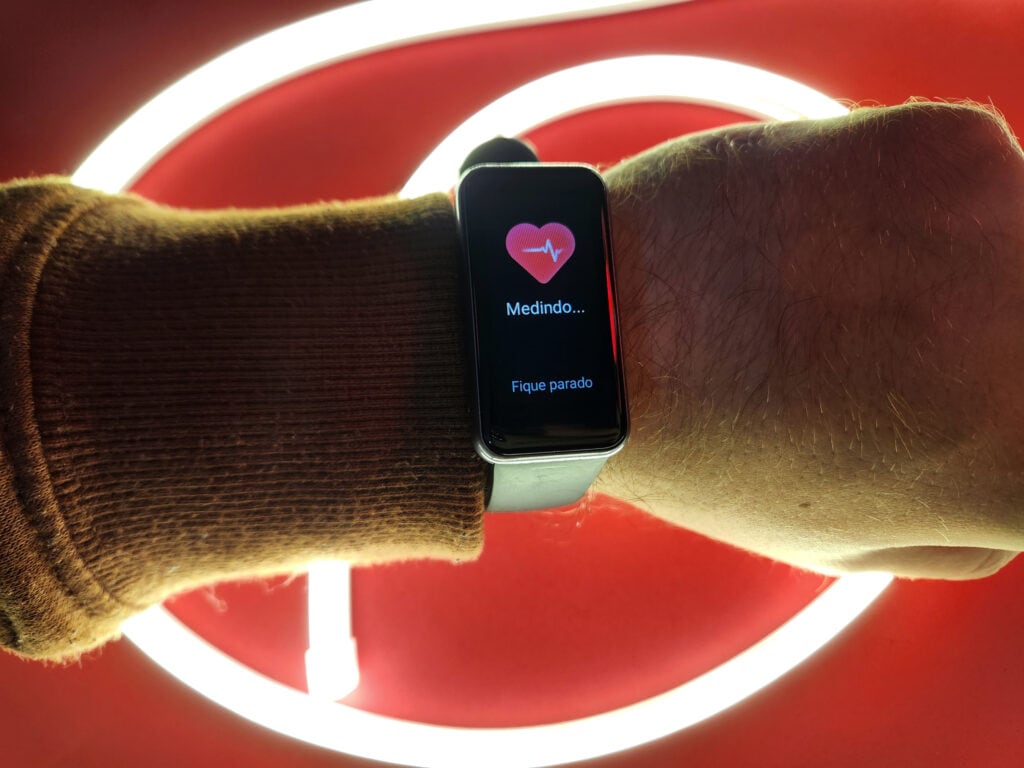 Realme band 2 no pulso de uma pessoa medindo batimentos cardiácos em fundo vermelho com fita de led neon