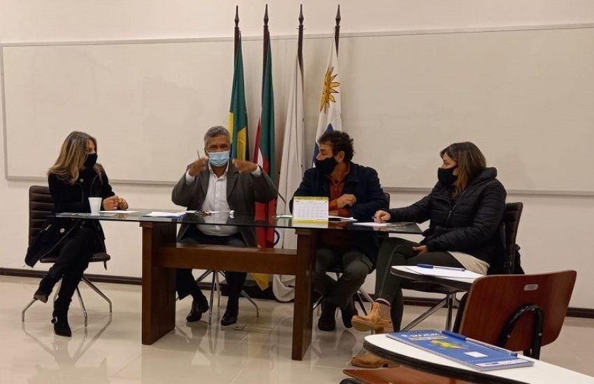 Imagem de cinco pessoas em reunião, usando máscaras, discutindo cargos políticos.