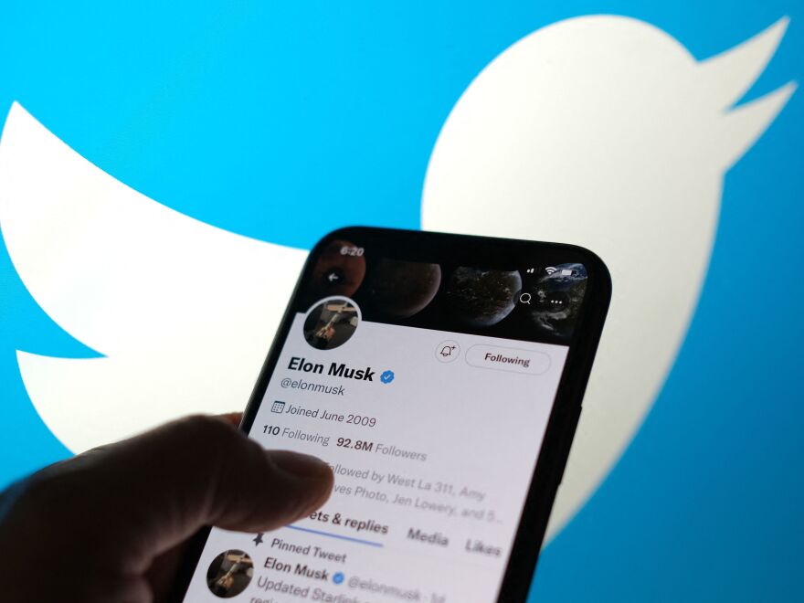 Smartphone with open elon musk account and blurred twitter logo in the background