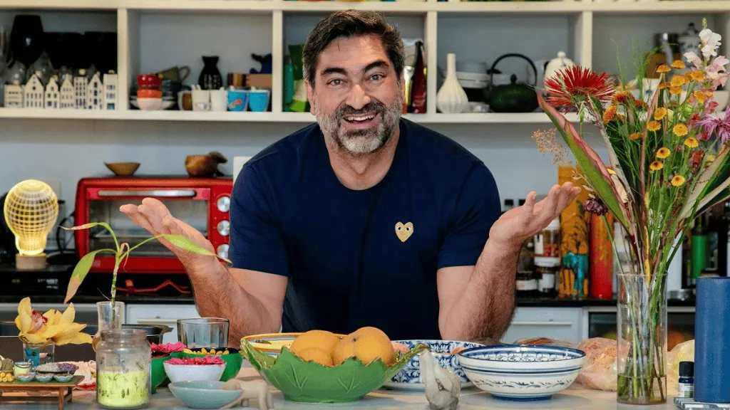 Gambar seorang pria tersenyum di dapur dengan bunga dan makanan, mempromosikan akses gratis ke saluran televisi.