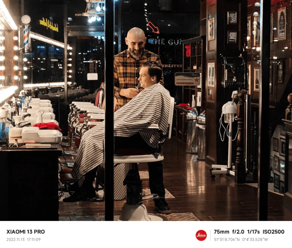 Câmera do xiaomi 13 pro pode ser a melhor em smartphones de 2023 Cabeleireiro aparando cabelo de cliente em barbearia moderna, ambiente com iluminação quente e decoração clássica, usando câmera xiaomi 13 pro com foco em detalhes.