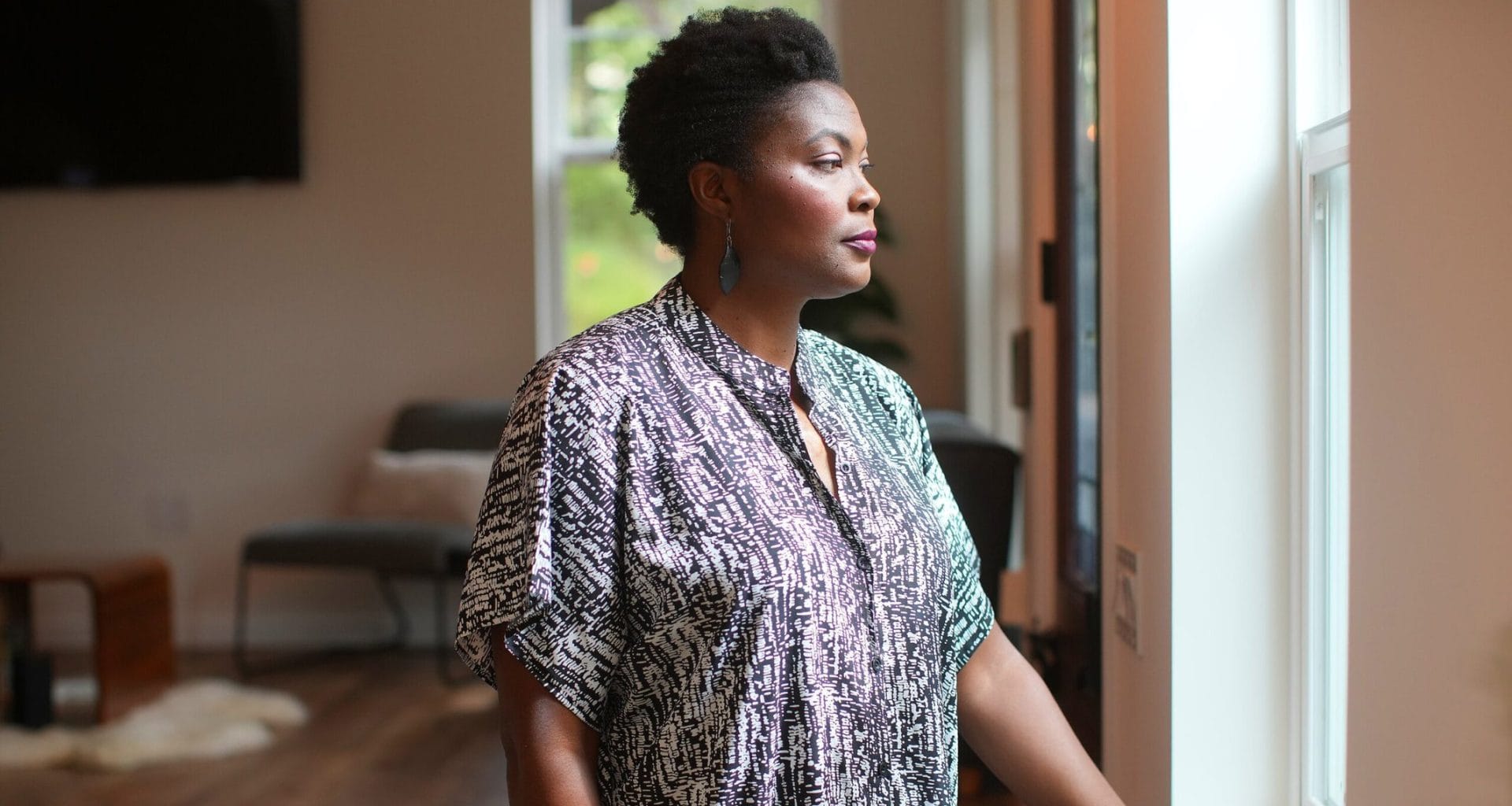 Mulher negra observando pela janela em imóvel alugado.