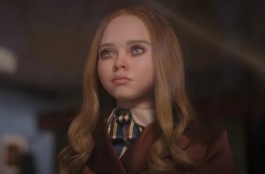 Texto alternativo: jovem com cabelo cacheado, vestido elegante e expressão pensativa, na cena de um filme.