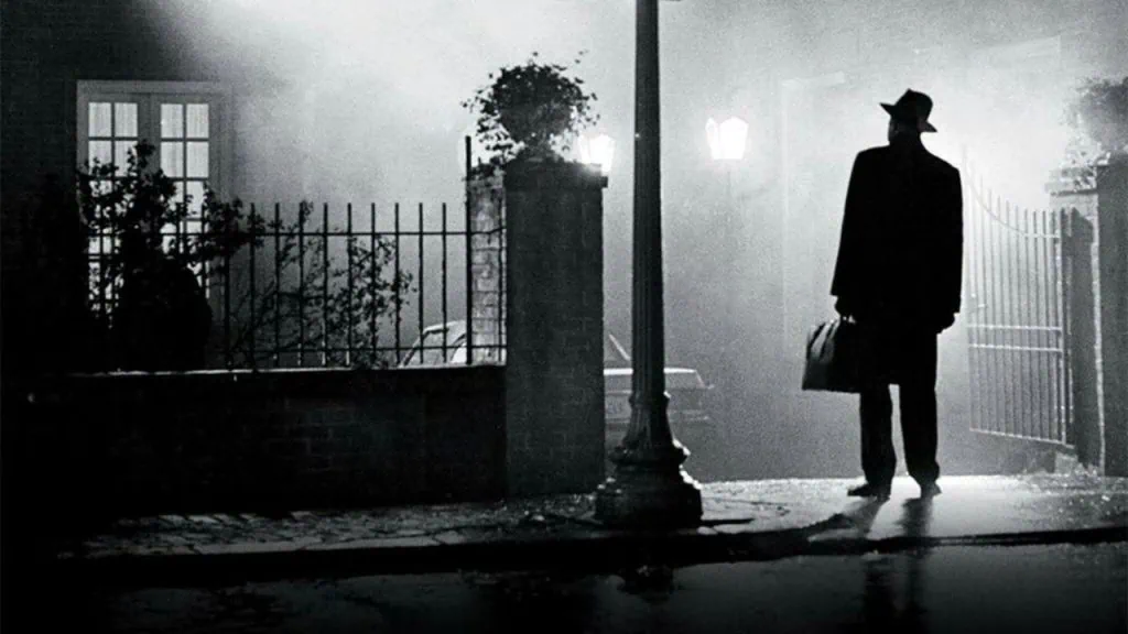 Os filmes de terror de 2023 mais aguardados! Cartaz do filme "o exorcista, preto e branco, em que o personagem padre merrin está olhando para a casa da família macneil.