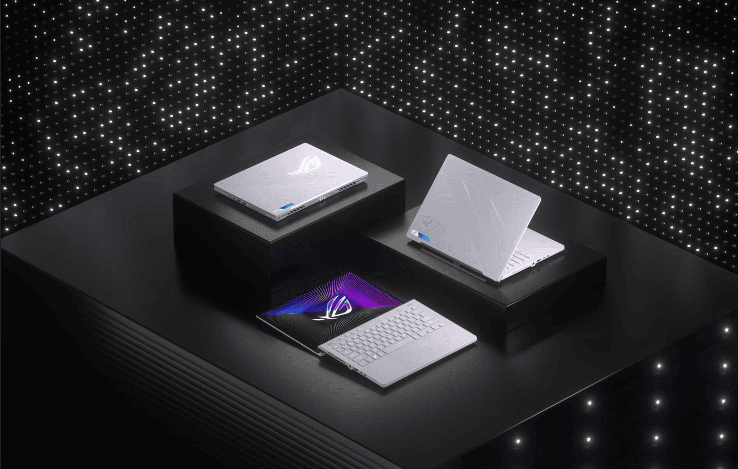 Imagem de três laptops rog em uma mesa com iluminação moderna.