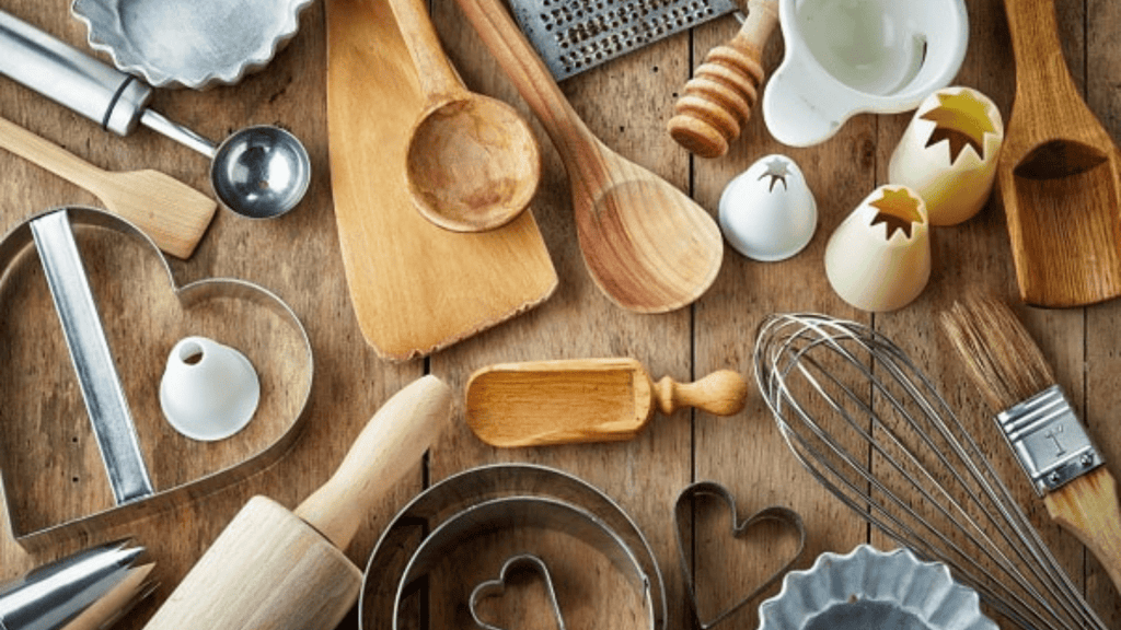 Utensilios de cocina de madera y metal sobre una encimera de madera, diversos artículos para la preparación de alimentos.