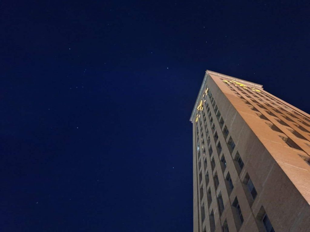 Cenário noturno com prédio alto e céu estrelado para destaque de tecnologia celular.