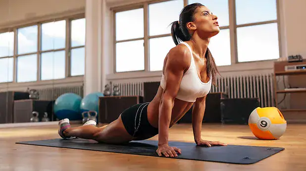 Mulher praticando alongamento no tapete em academia.