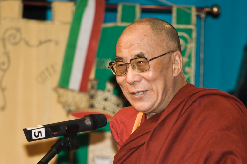 Imagem do atual dalai lama, tenzin gyatso falando em um microfone.