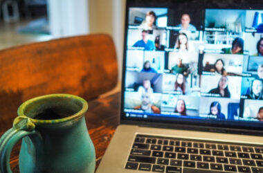 Pessoa com uma xícara azul com café está na frente de notebook assistindo a um curso online
