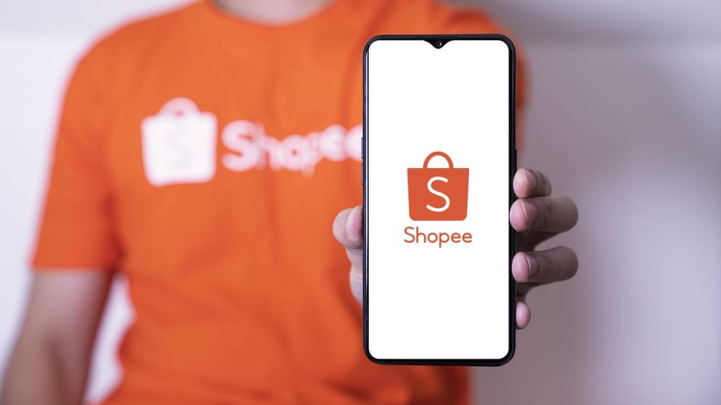 Compras internacionais online valem a pena? Um guia completo Na foto há um homem segurando um aparelho celular, nele é possível ver o símbolo da shopee.
