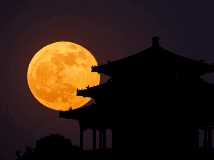 Imagem da lua cheia próxima a uma pagoda tradicional chinesa.