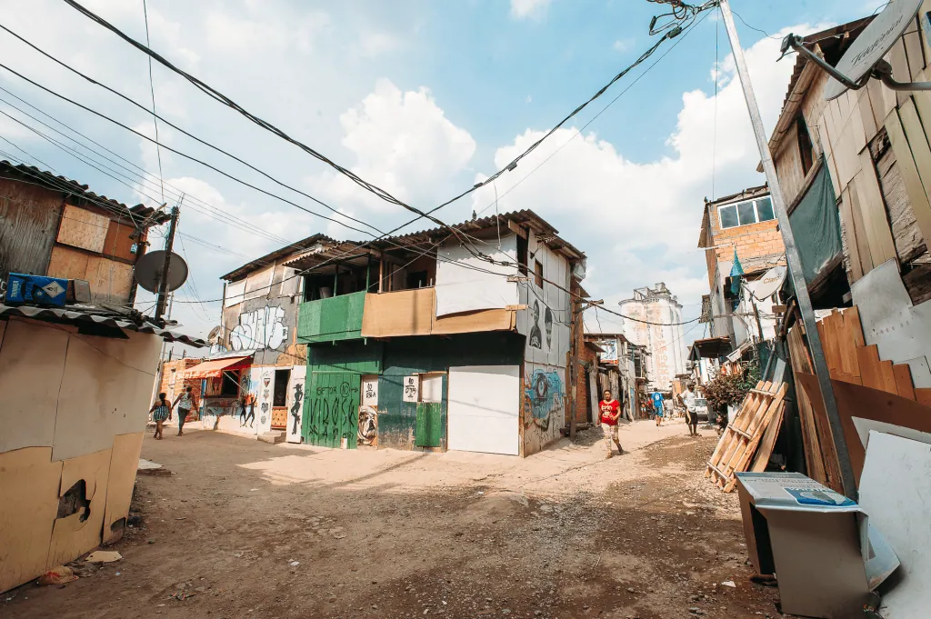 Saiba o que o censo 2022 revela sobre a população do brasil Déficit de domicílio t alt casa ao centro, que fica próximo a rua sem asfalto, com chão de terra; as cores predominantes da casa são verde e branco