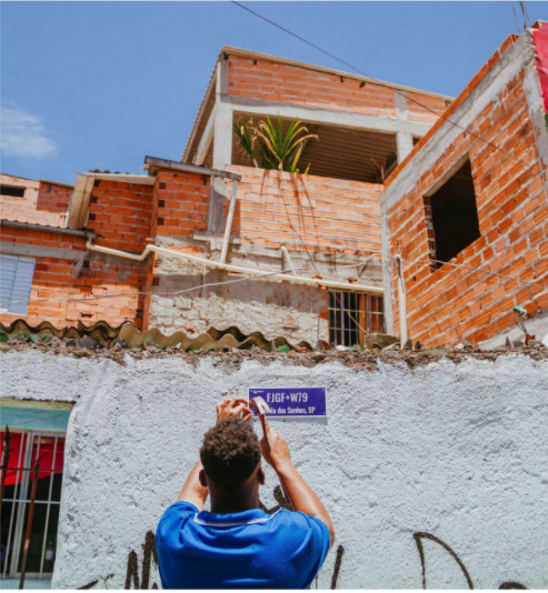 Colaborador do naporta fixando uma placa com plus codes na favela dos sonhos. Imagem: google