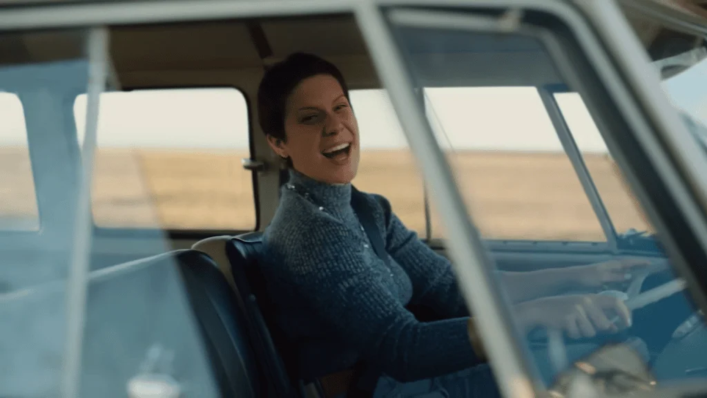 Mulher sorrindo no volante de um carro clássico em estrada rural, aventura e tecnologia.