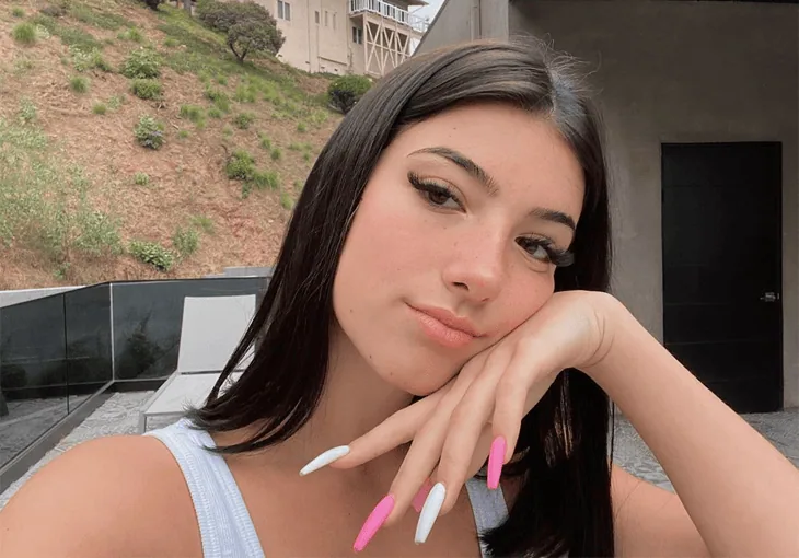 Os 10 maiores influencers do mundo em 2023 Maquiagem natural, unhas decoradas com esmalte rosa e branco, jovem mulher com rosto sereno ao ar livre.