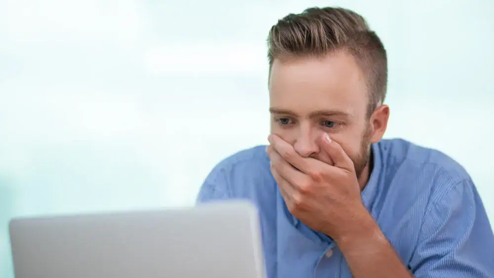 Homem assustado usando notebook, expressão de surpresa ou preocupação.