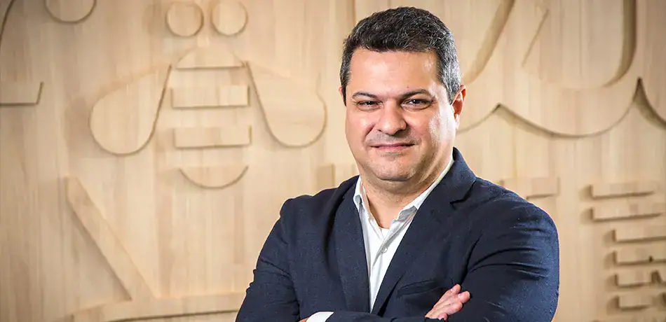 Executivo de terno com braços cruzados em ambiente corporativo sofisticado.