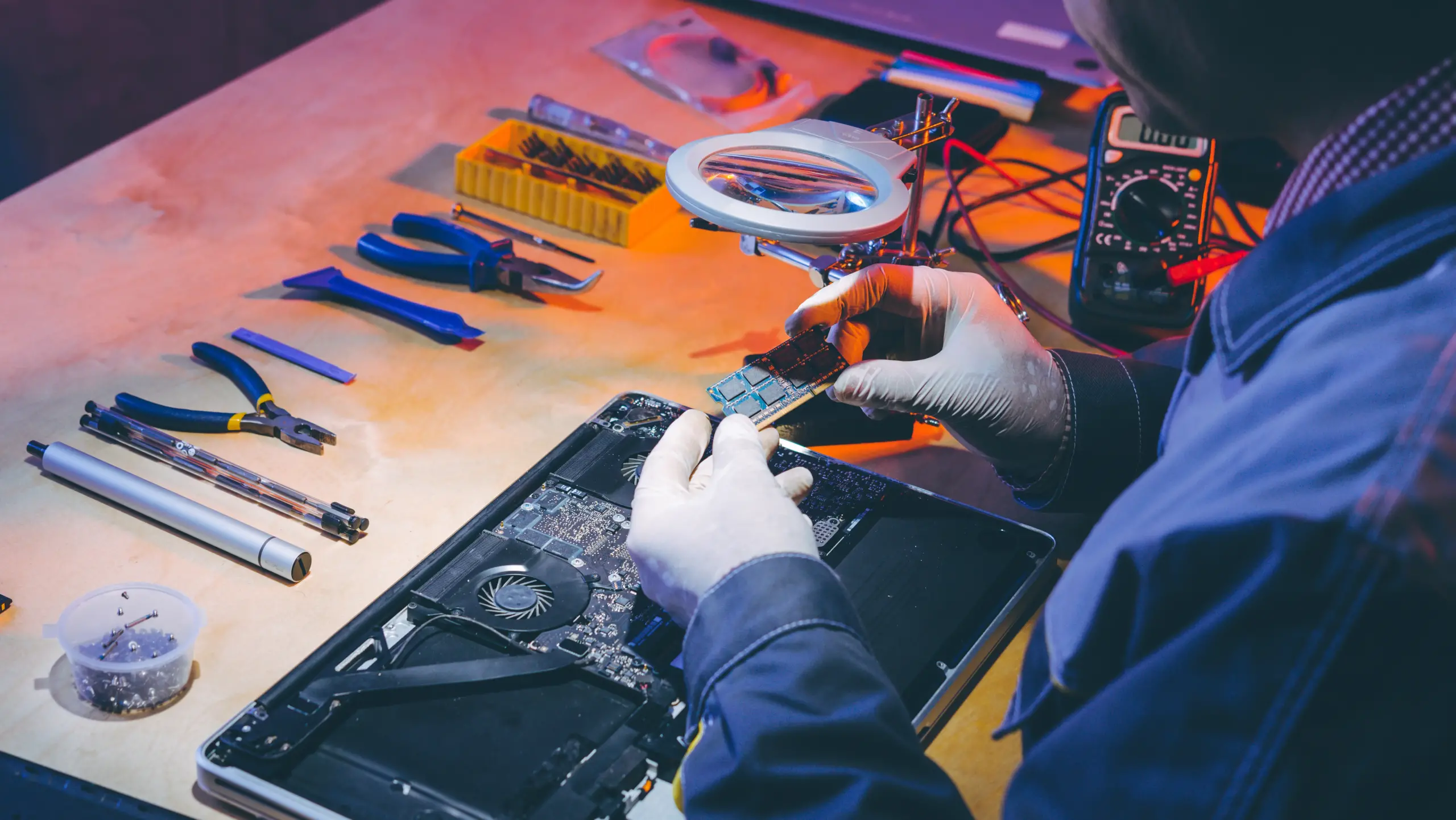 Produto há mais de 30 dias no conserto? Você pode receber um novo, segundo o cdc Na foto é possível ver uma mesa marrom com diversas peças e ferramentas. A direita, uma pessoa está fazendo o conserto de um notebook.