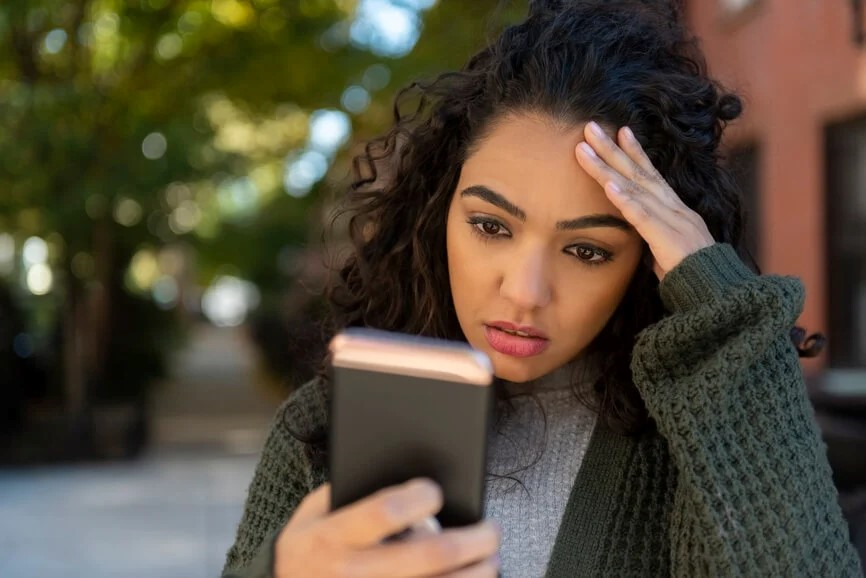 Imagem de uma jovem com um celular na mão direita e a mão esquerda na cabeça, expressando estresse ou preocupação - as ligações telefônicas incessantes e desnecessárias podem gerar estresse no dia a dia (imagem: google)