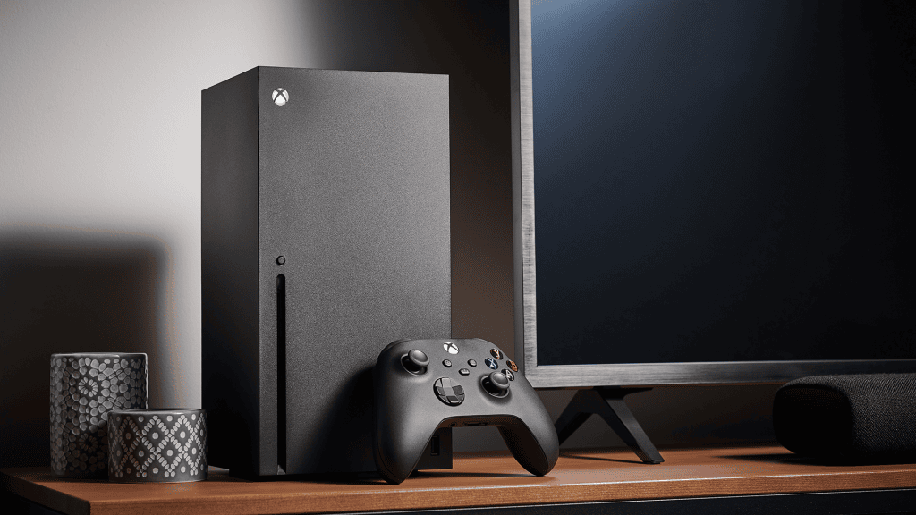 Xbox series x com controle ao lado, monitor e alto-falante em ambiente de tecnologia.