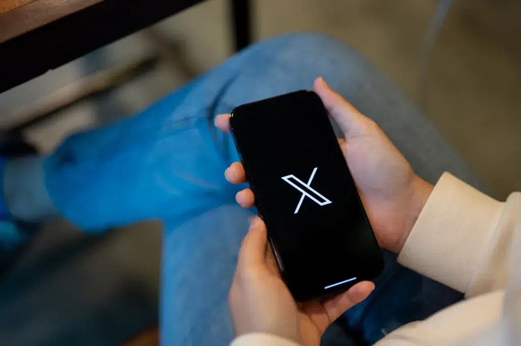 Na imagem, há uma pessoa segurando um celular com o aplicativo x na tela.