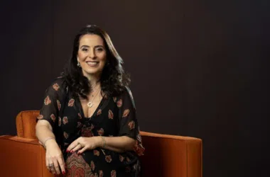 Mulher sorrindo sentada em sofá laranja, estilo profissional, em ambiente de estúdio.