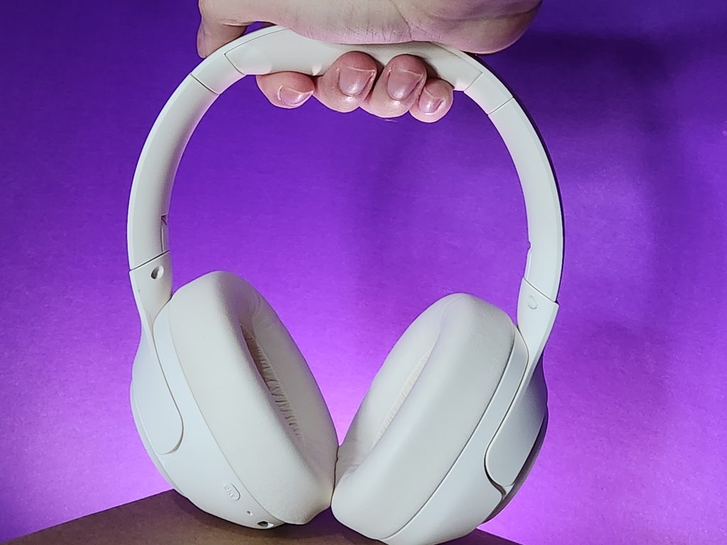 Fone de ouvido wireless branco com almofadas macias contra fundo roxo.