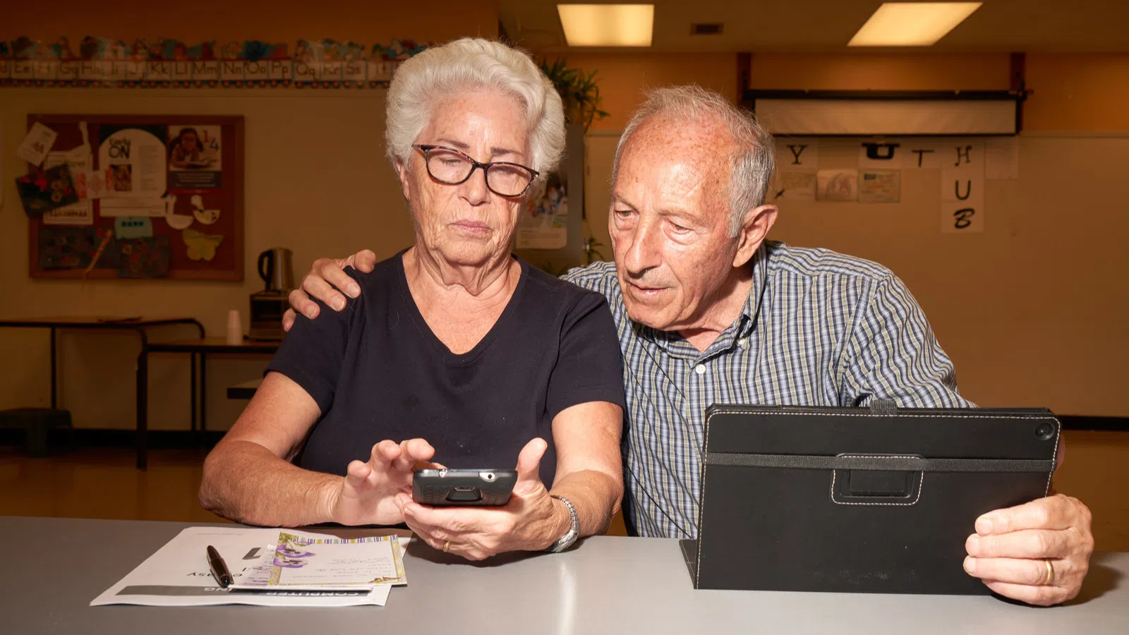 Avó e avô usando smartphone e tablet em ambiente escolar, tecnologia e idosos.