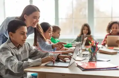 Tecnologia na educação, crianças usando laptops e professora auxiliando, ensino digital, sala de aula moderna, aprendizado interativo.