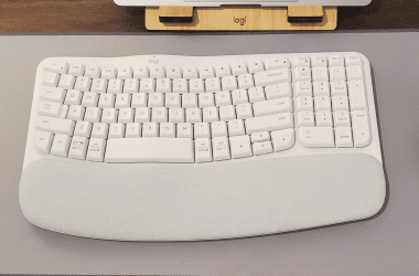 Teclado branco logitech com suporte ergonômico e mouse na mesa de escritório.