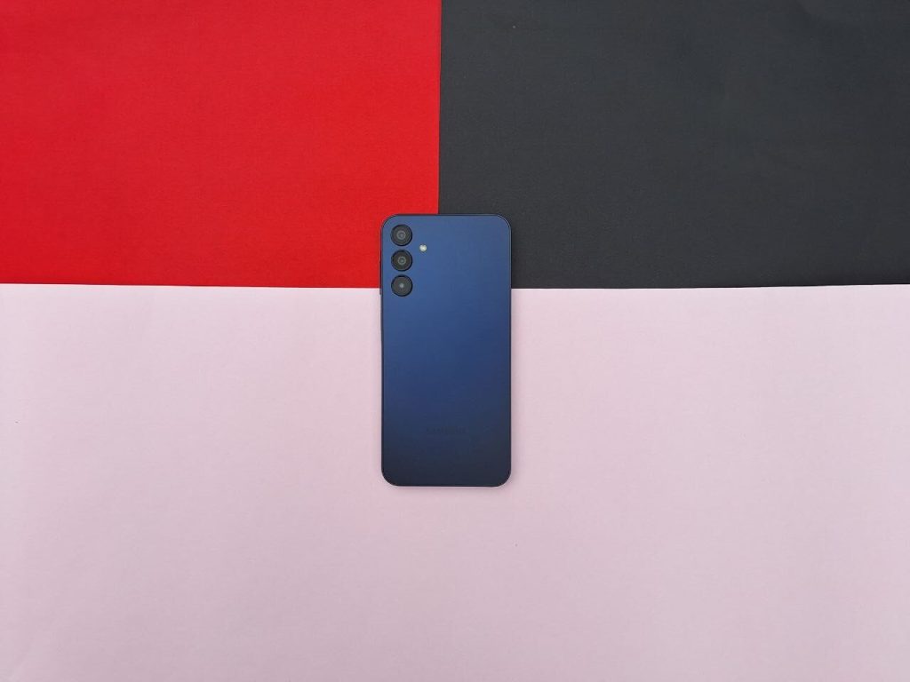 Обзор: Galaxy A15 5G, еще один хороший вариант среднего класса Задняя часть Galaxy A15 5G темно-синего цвета на черном, красном и фиолетовом фоне