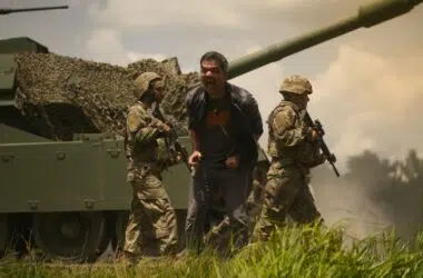 Homem gritando com soldados militares ao fundo durante exercício militar ao ar livre.