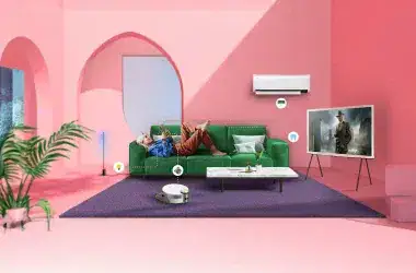 Casa com interior cor de rosa, com uma mulher sentada no sofá controlando seus eletrodomésticos pelo celular com o smartthings da samsung