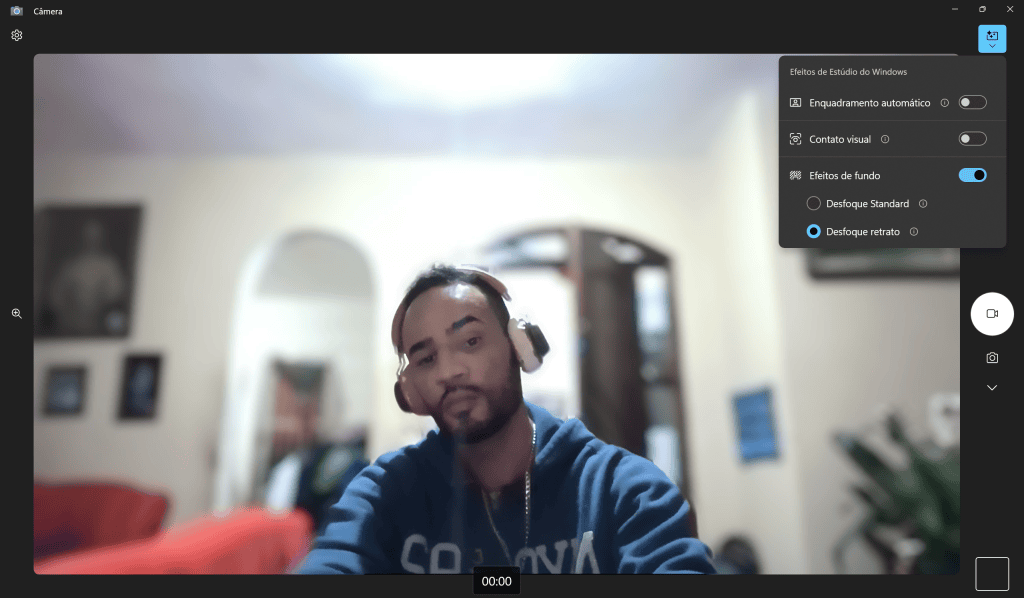 Foto de um homem com headset fazendo selfie, fundo borrado, em ambiente doméstico, com foco em tecnologia e vídeos online.