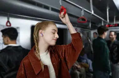 Confortável jovem usando fones de ouvido e segurando alça no metrô, desfrutando música e momento de relaxamento.