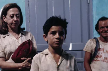 1. Mulher idosa e dois jovens sentados em ambiente interior com porta de fundo.