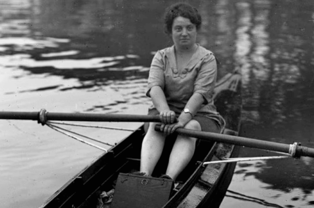 Mulher remando em barco clássico no rio, preto e branco.