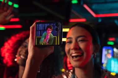 Câmera de smartphone captura grupo de jovens se divertindo em festa com luzes neon vibrantes.