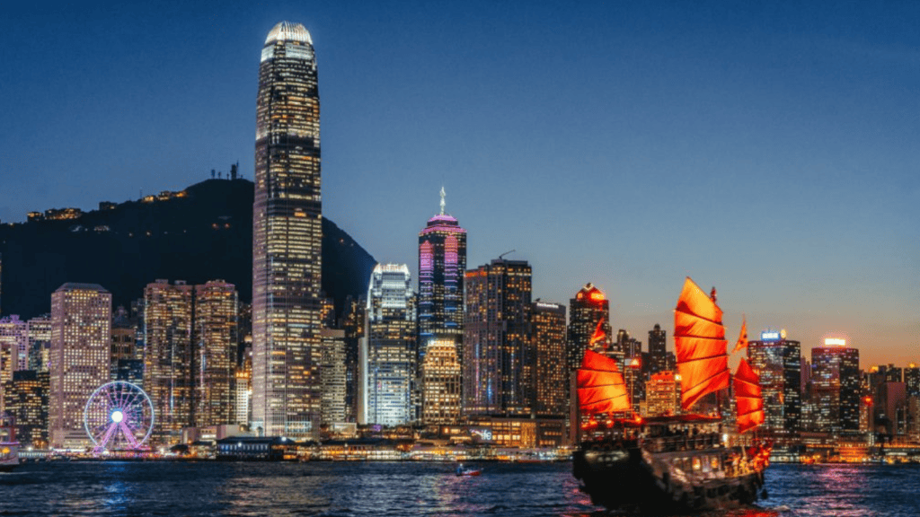 1. Horizonte de hong kong com arranha-céus iluminados e barco tradicional voando com velas vermelhas.